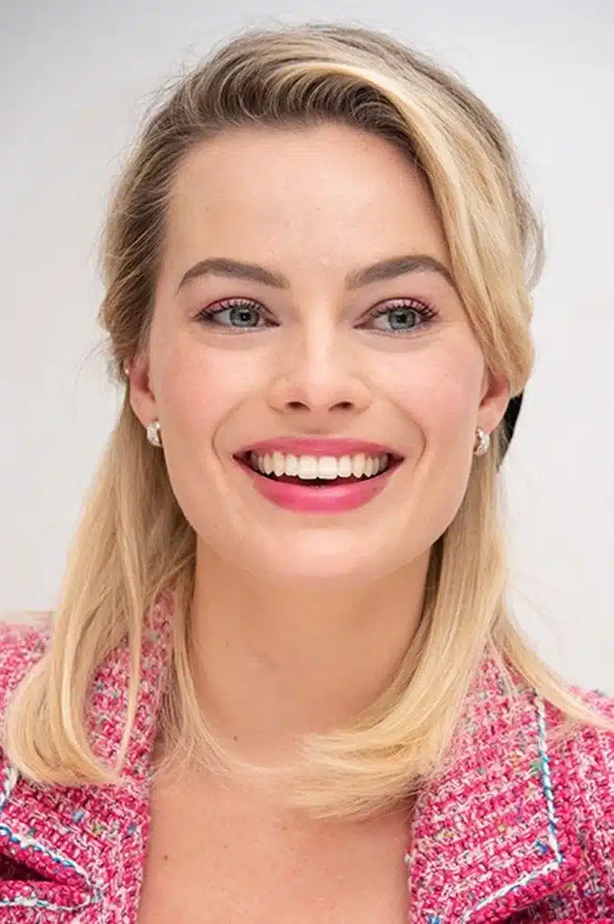 “Margot Robbie in red-carpet setting with radiant bright smile.”