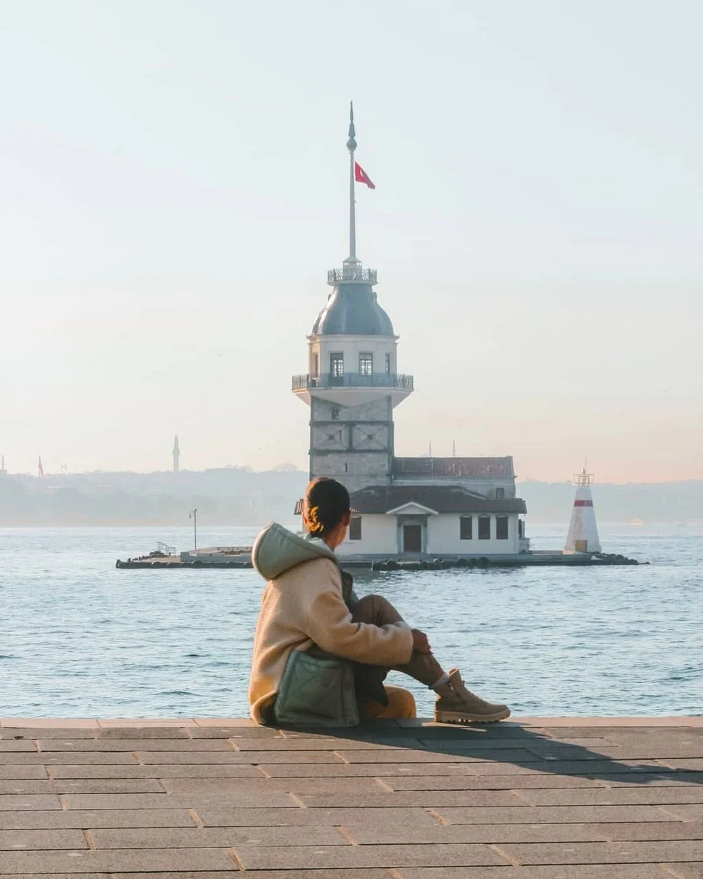 Woman sitting by the Bosphorus with Maiden's Tower in the distance