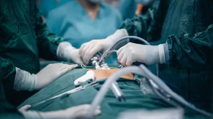 Gloved surgical team working with instruments over a draped patient in an operating room