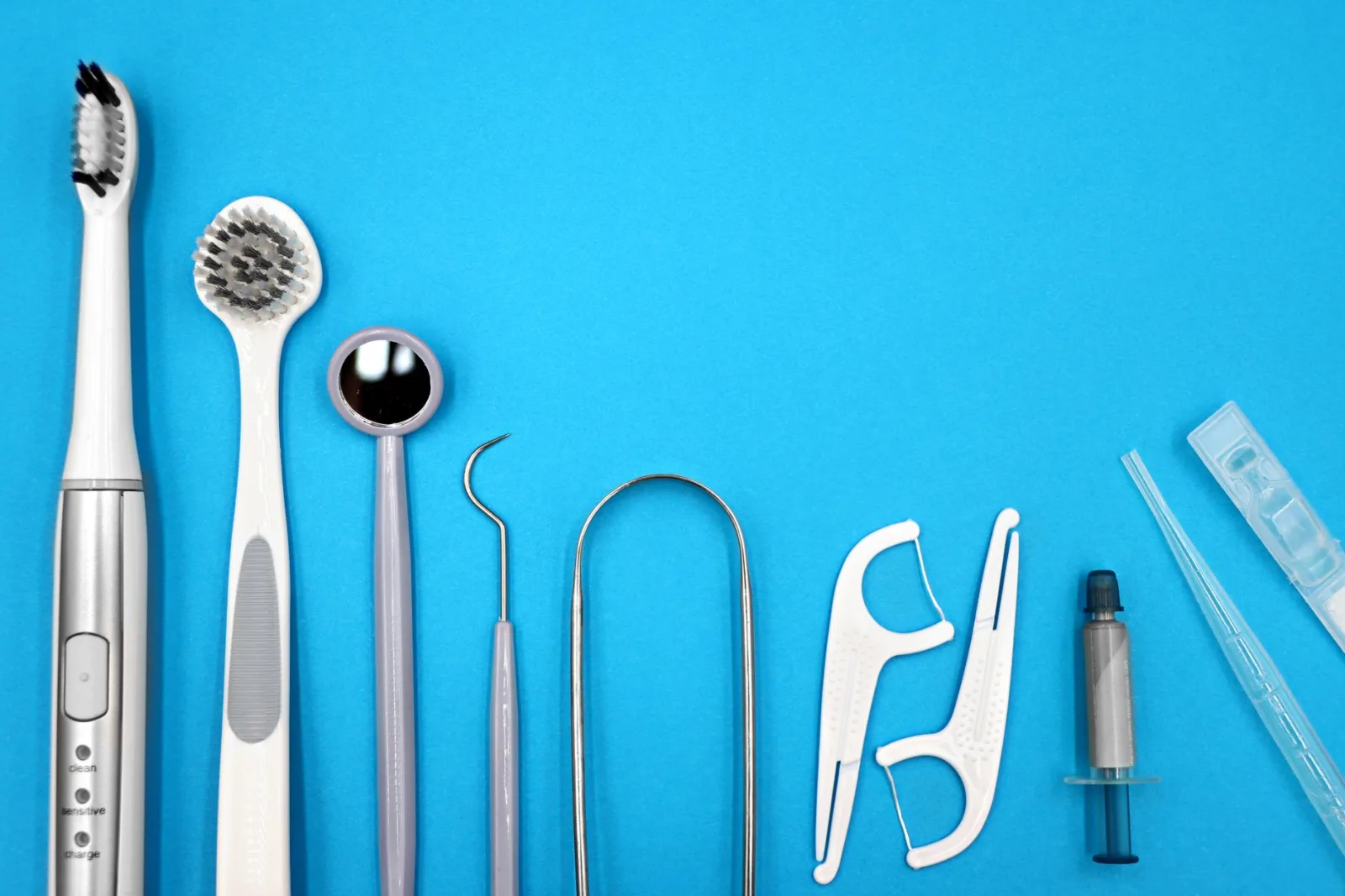 Oral hygiene tools laid out in a row: an electric toothbrush, single-tuft brush, dental mirror, probe, interdental picks and floss